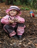 Girl sitting in dirt wearing Muddy Buddy waterproof coveralls in pink