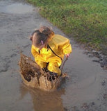 Girl splashing in mud puddle wearing Muddy Buddy waterproof coveralls in yellow
